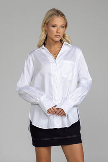 The distinguished Blak Atlas Shirt in crisp white combines every thing you need in a refined silhouette. Features include a v-neckline with collar, button-through front, and long sleeves culminating in deep cuffs with elegant tie closures. A discreet patch pocket adds functionality, while the back yoke with inverted box pleat ensures graceful movement. Sophisticated side-splits and a curved hemline complete this versatile piece, suitable for both professional and casual occasions.
Fabric composition -Cotton