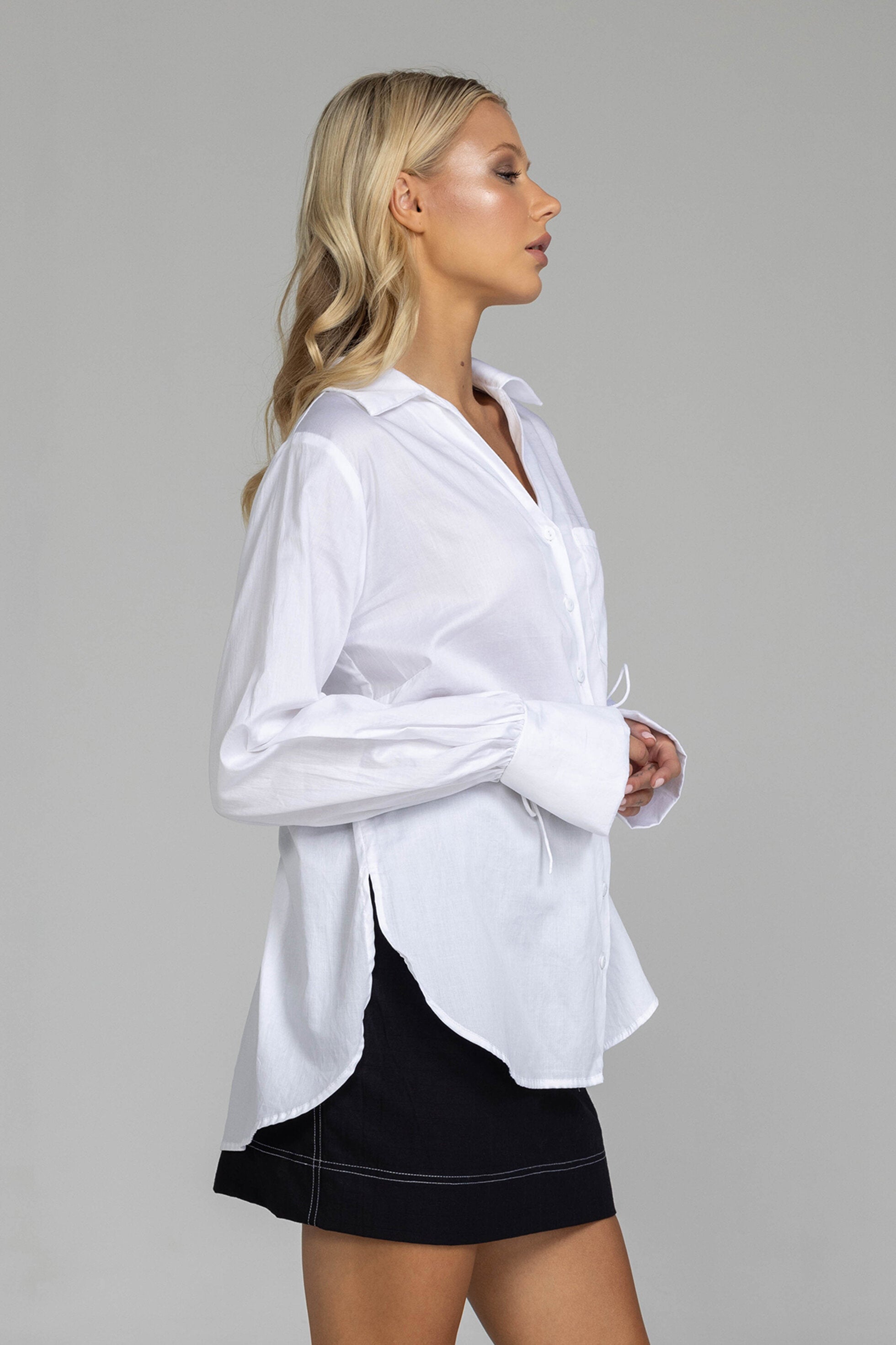 The distinguished Blak Atlas Shirt in crisp white combines every thing you need in a refined silhouette. Features include a v-neckline with collar, button-through front, and long sleeves culminating in deep cuffs with elegant tie closures. A discreet patch pocket adds functionality, while the back yoke with inverted box pleat ensures graceful movement. Sophisticated side-splits and a curved hemline complete this versatile piece, suitable for both professional and casual occasions.
Fabric composition -Cotton
