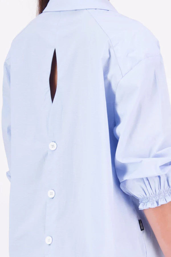 The N-E-S Fara Shirt blends classic tailoring with soft, modern touches. Featuring 7/8 sleeves with three layers of shirring at the cuffs, a traditional collar flowing into an open V-neck and centre front pleat. The drop-back design reveals a cross-over keyhole and centre back button detail. Style the sleeves your way—worn down, ruched up, or tucked under—for versatile, effortless dressing.
Composition: Sky (fine seersucker) - cotton, spandex | Oyster grey stripe cotton, polyamide, elastine.