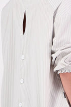 The N-E-S Fara Shirt blends classic tailoring with soft, modern touches. Featuring 7/8 sleeves with three layers of shirring at the cuffs, a traditional collar flowing into an open V-neck and centre front pleat. The drop-back design reveals a cross-over keyhole and centre back button detail. Style the sleeves your way—worn down, ruched up, or tucked under—for versatile, effortless dressing.
Composition: Sky (fine seersucker) - cotton, spandex | Oyster grey stripe cotton, polyamide, elastine.