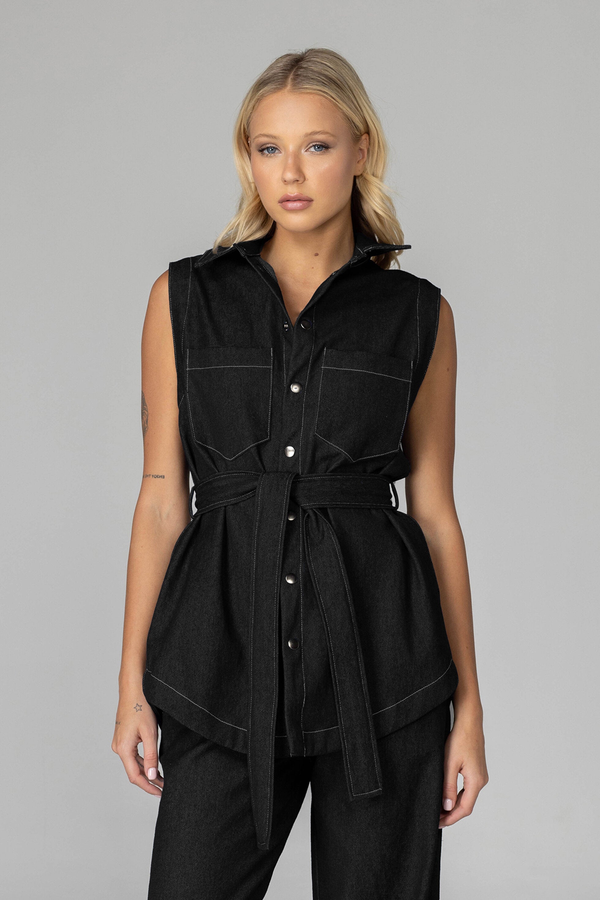The BLAK Kent Vest offers quality cotton denim with traditional white topstitching in a comfortable relaxed fit. Features include easy-to-use dome closures, a flattering collar, and practical front pockets for your essentials. The included tie belt helps create your ideal silhouette, while the thoughtfully designed back with inverted pleat ensures both comfort and movement. 