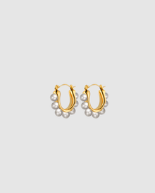 Margot Earrings by Castel & Co feature a softly sculpted gold-plated stainless steel hoop finished with a luminous imitation pearl drop. Designed to feel both modern and timeless, they bring a refined edge to everyday styling while also suiting occasion wear. Measuring 2.4 x 2.6 cm with a secure hinge closure. Lightweight (10g), waterproof, and hypoallergenic.