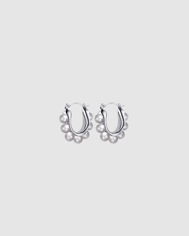 Margot Earrings by Castel & Co feature a softly sculpted gold-plated stainless steel hoop finished with a luminous imitation pearl drop. Designed to feel both modern and timeless, they bring a refined edge to everyday styling while also suiting occasion wear. Measuring 2.4 x 2.6 cm with a secure hinge closure. Lightweight (10g), waterproof, and hypoallergenic.