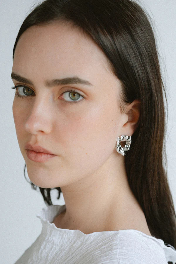 Modern and sculptural, the Castel & Co Remi Earrings in polished silver feature an open, organic form with a textured finish. Their irregular shape adds depth and edge, while the cool silver tone brings a sleek, contemporary feel. A striking statement stud that balances artistry with everyday versatility.

Material: Stainless steel
Closure Type: Stud
Earring Size: 3 x 2.4 cm
Waterproof and hypoallergenic
Weight: 8g