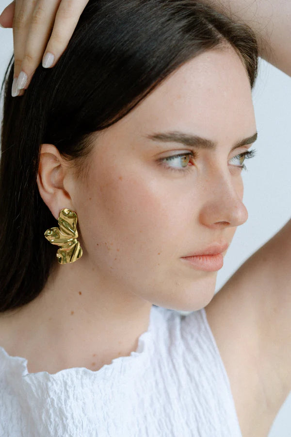 Sculptural and dramatic, the Castel & Co Sienna Earrings feature fluid, folded curves in radiant gold plating. Their bold silhouette and organic form create a striking sense of movement, designed to frame the face with modern artistry. A statement earring that embodies elegance with an edge.

Material: Stainless steel, Gold plating
Closure Type: Stud
Earrings Size: 4.5 x 2.5 cm
Waterproof and hypoallergenic
Weight: 7g