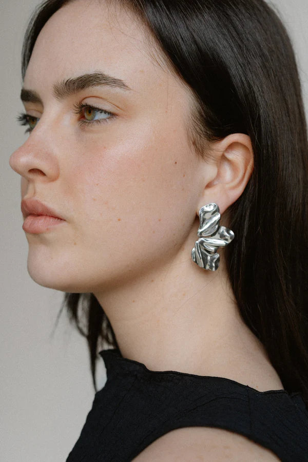 Sculptural and dramatic, the Castel & Co Sienna Earrings feature fluid, folded curves in radiant gold plating. Their bold silhouette and organic form create a striking sense of movement, designed to frame the face with modern artistry. A statement earring that embodies elegance with an edge.

Material: Stainless steel, Gold plating
Closure Type: Stud
Earrings Size: 4.5 x 2.5 cm
Waterproof and hypoallergenic
Weight: 7g