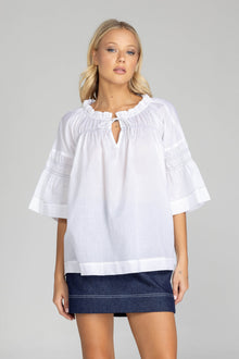The distinguished BLAK Thea Top presents an elegant interplay of white fabric and refined black stitching. Crafted from premium cotton voile, this sophisticated piece features a gracefully gathered round neckline complemented by a tasteful front keyhole with delicate ties. The artfully designed shirt sleeves showcase meticulous shirring details, echoed in the thoughtful shirring embellishments adorning both the upper front and back. The silhouette extends precisely to mid-hip, concluding with a pristine str