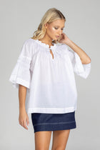 The distinguished BLAK Thea Top presents an elegant interplay of white fabric and refined black stitching. Crafted from premium cotton voile, this sophisticated piece features a gracefully gathered round neckline complemented by a tasteful front keyhole with delicate ties. The artfully designed shirt sleeves showcase meticulous shirring details, echoed in the thoughtful shirring embellishments adorning both the upper front and back. 