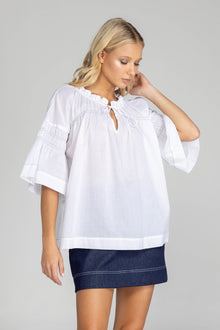 The distinguished BLAK Thea Top presents an elegant interplay of white fabric and refined black stitching. Crafted from premium cotton voile, this sophisticated piece features a gracefully gathered round neckline complemented by a tasteful front keyhole with delicate ties. The artfully designed shirt sleeves showcase meticulous shirring details, echoed in the thoughtful shirring embellishments adorning both the upper front and back. 
