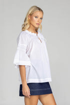 The distinguished BLAK Thea Top presents an elegant interplay of white fabric and refined black stitching. Crafted from premium cotton voile, this sophisticated piece features a gracefully gathered round neckline complemented by a tasteful front keyhole with delicate ties. The artfully designed shirt sleeves showcase meticulous shirring details, echoed in the thoughtful shirring embellishments adorning both the upper front and back. 
