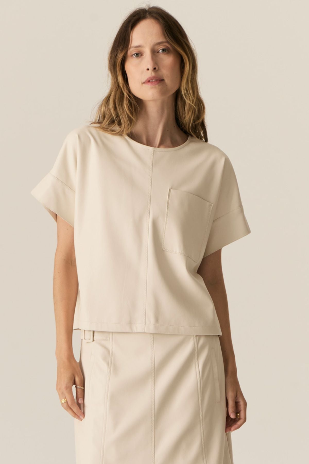 Featuring a soft faux leather in a fresh Ecru shade, the POL Belmond Top has a boxy, t-shirt inspired silhouette.

-Round neckline.
-Covered button fastening at the back neck.
-Dropped armholes.
-Short sleeves finish in a cuff with covered button fastening.