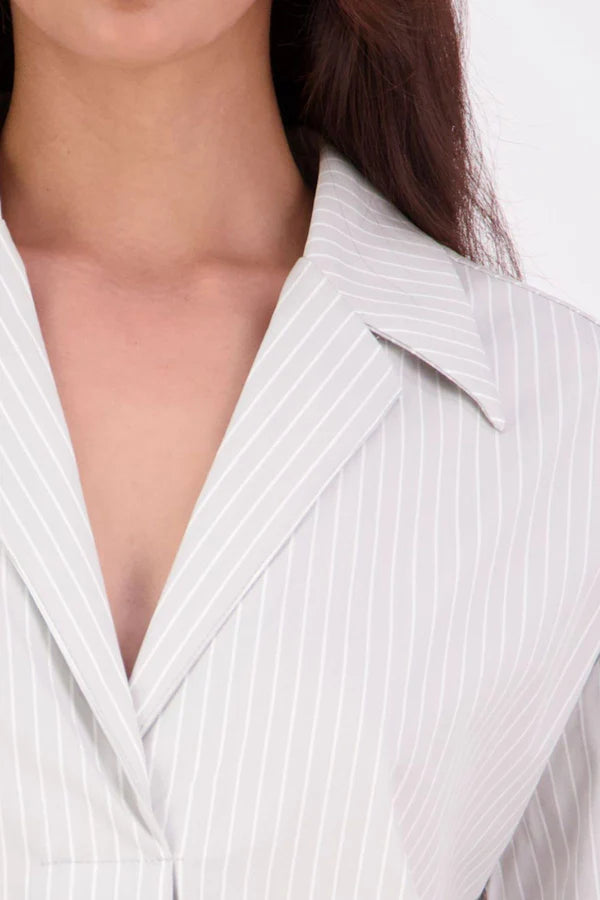 The N-E-S Fara Shirt blends classic tailoring with soft, modern touches. Featuring 7/8 sleeves with three layers of shirring at the cuffs, a traditional collar flowing into an open V-neck and centre front pleat. The drop-back design reveals a cross-over keyhole and centre back button detail. Style the sleeves your way—worn down, ruched up, or tucked under—for versatile, effortless dressing.
Composition: Sky (fine seersucker) - cotton, spandex | Oyster grey stripe cotton, polyamide, elastine.