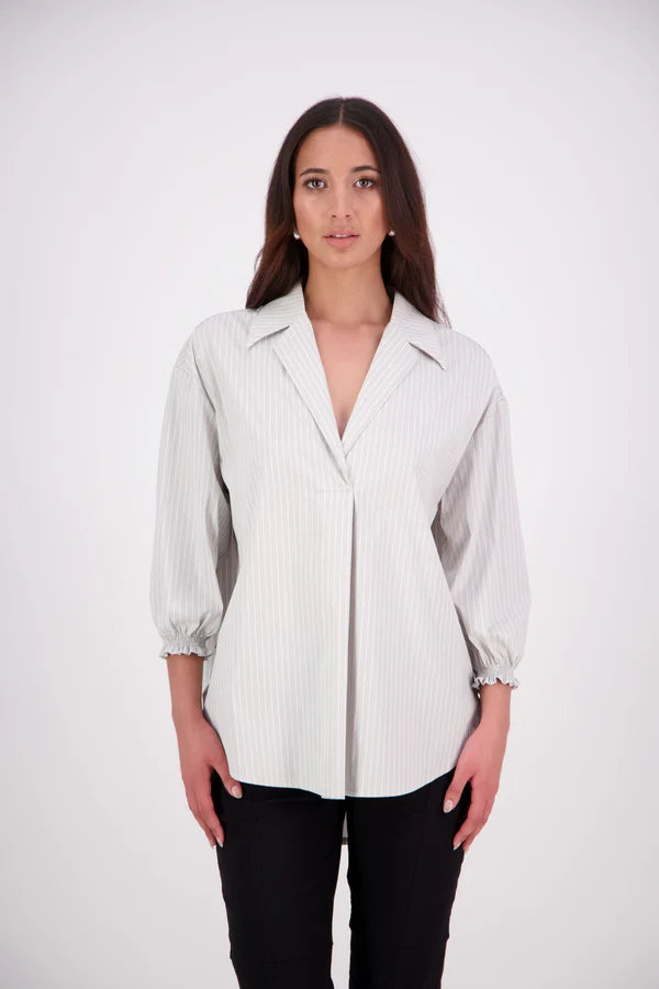 The N-E-S Fara Shirt blends classic tailoring with soft, modern touches. Featuring 7/8 sleeves with three layers of shirring at the cuffs, a traditional collar flowing into an open V-neck and centre front pleat. The drop-back design reveals a cross-over keyhole and centre back button detail. Style the sleeves your way—worn down, ruched up, or tucked under—for versatile, effortless dressing.
Composition: Sky (fine seersucker) - cotton, spandex | Oyster grey stripe cotton, polyamide, elastine.