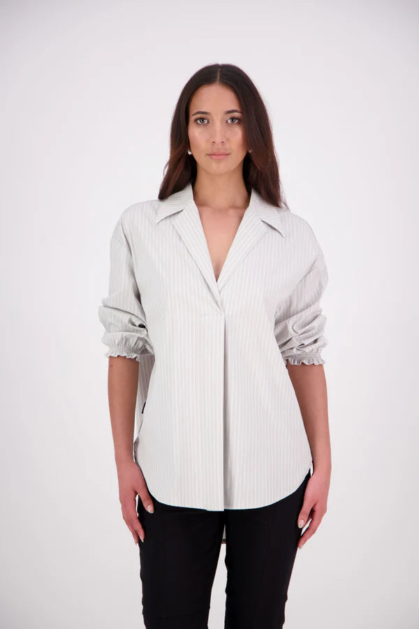 The N-E-S Fara Shirt blends classic tailoring with soft, modern touches. Featuring 7/8 sleeves with three layers of shirring at the cuffs, a traditional collar flowing into an open V-neck and centre front pleat. The drop-back design reveals a cross-over keyhole and centre back button detail. Style the sleeves your way—worn down, ruched up, or tucked under—for versatile, effortless dressing.
Composition: Sky (fine seersucker) - cotton, spandex | Oyster grey stripe cotton, polyamide, elastine.