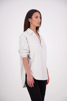 The N-E-S Fara Shirt blends classic tailoring with soft, modern touches. Featuring 7/8 sleeves with three layers of shirring at the cuffs, a traditional collar flowing into an open V-neck and centre front pleat. The drop-back design reveals a cross-over keyhole and centre back button detail. Style the sleeves your way—worn down, ruched up, or tucked under—for versatile, effortless dressing.
Composition: Sky (fine seersucker) - cotton, spandex | Oyster grey stripe cotton, polyamide, elastine.
