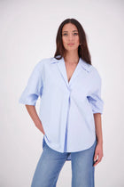 The N-E-S Fara Shirt blends classic tailoring with soft, modern touches. Featuring 7/8 sleeves with three layers of shirring at the cuffs, a traditional collar flowing into an open V-neck and centre front pleat. The drop-back design reveals a cross-over keyhole and centre back button detail. Style the sleeves your way—worn down, ruched up, or tucked under—for versatile, effortless dressing.
Composition: Sky (fine seersucker) - cotton, spandex | Oyster grey stripe cotton, polyamide, elastine.