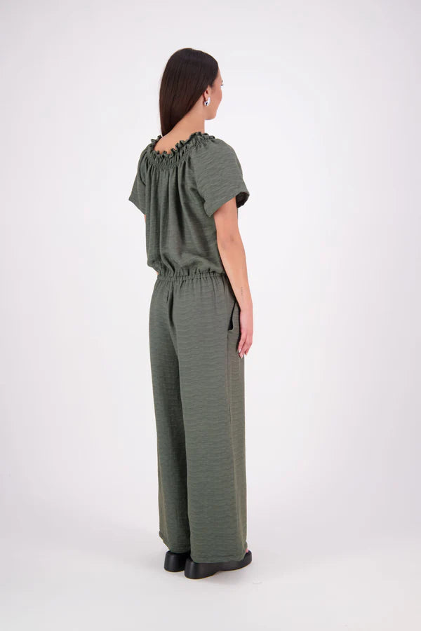 The N-E-S Muses Jumpsuit features a shirred off-the-shoulder top with cap sleeves, an elasticated back waist, and a self-drawcord front for a flattering, adjustable fit. The lower half mirrors the relaxed fit of our Lounge Jumpsuit, with angled seams, centre front detailing, and practical front pockets